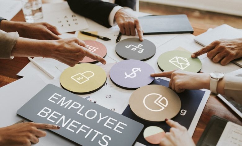Team discussing employee benefits, with color-coded circular icons for benefits like salary, security, and perks on a table.
