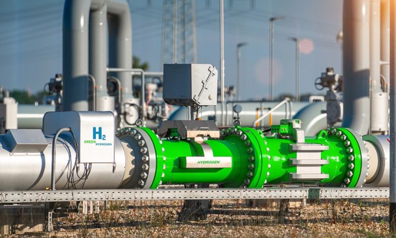 Industrial hydrogen pipeline system with bright green piping and valves at a processing facility outdoors, with equipment in the background.